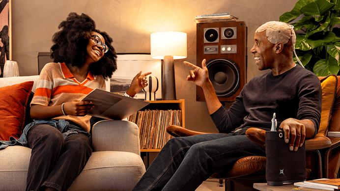 Man wearing Optune Gio points playfully at a woman as they both relax in a living room.